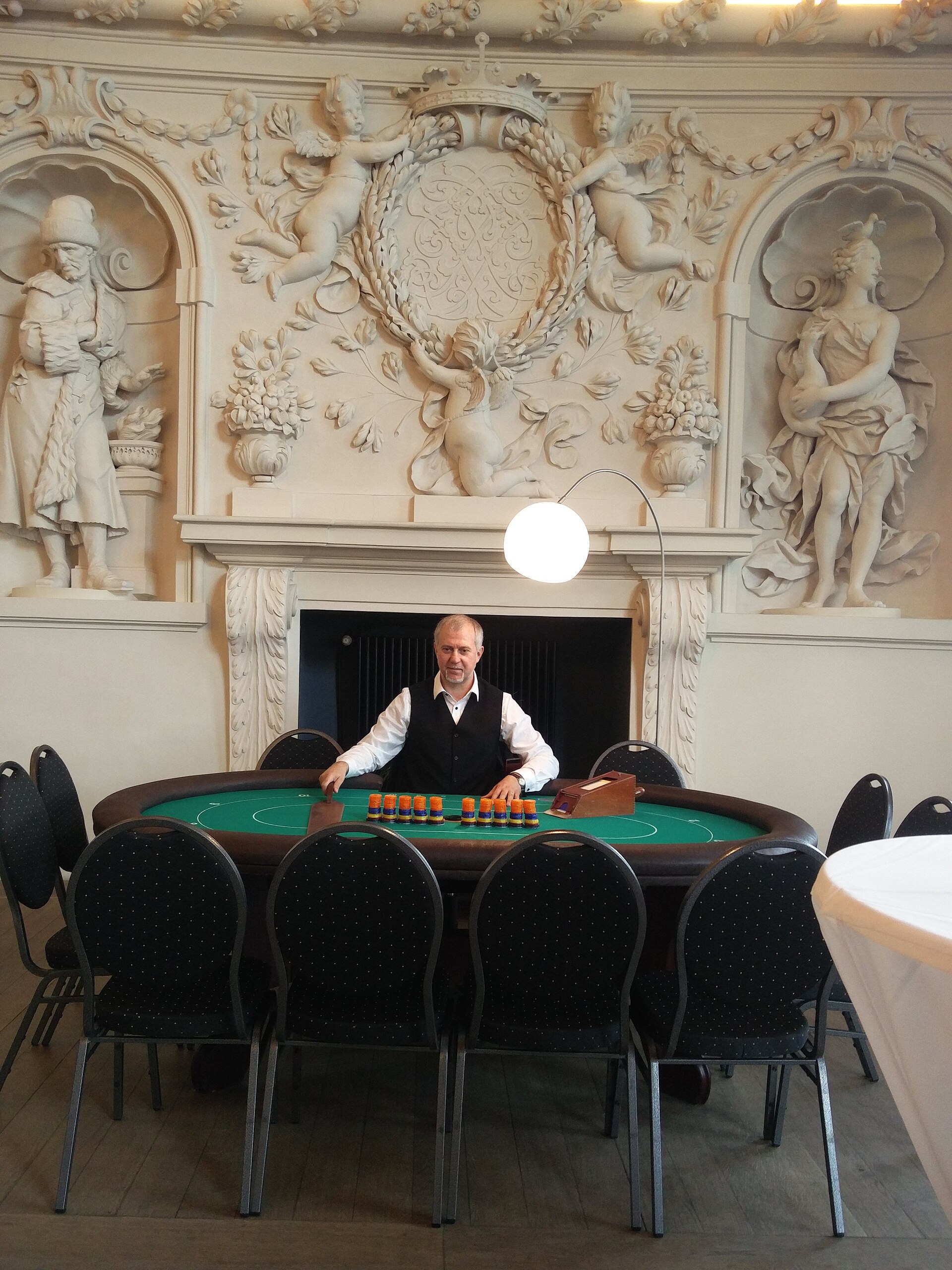 Casino dealer seated at a green felt card table with chips